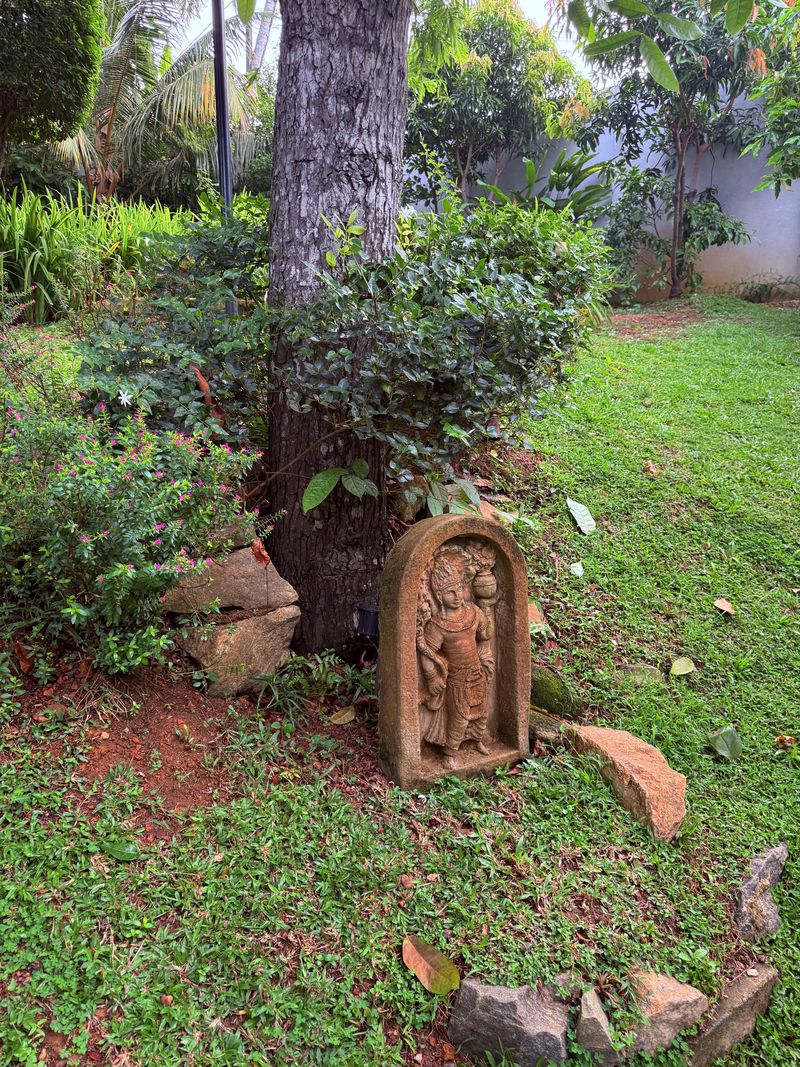 A carved stone figure at the foot of a garden tree