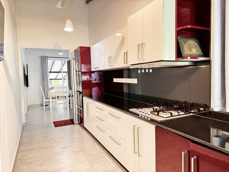 The long, fully equipped dry kitchen with white and red cabinets, opening onto the dining area